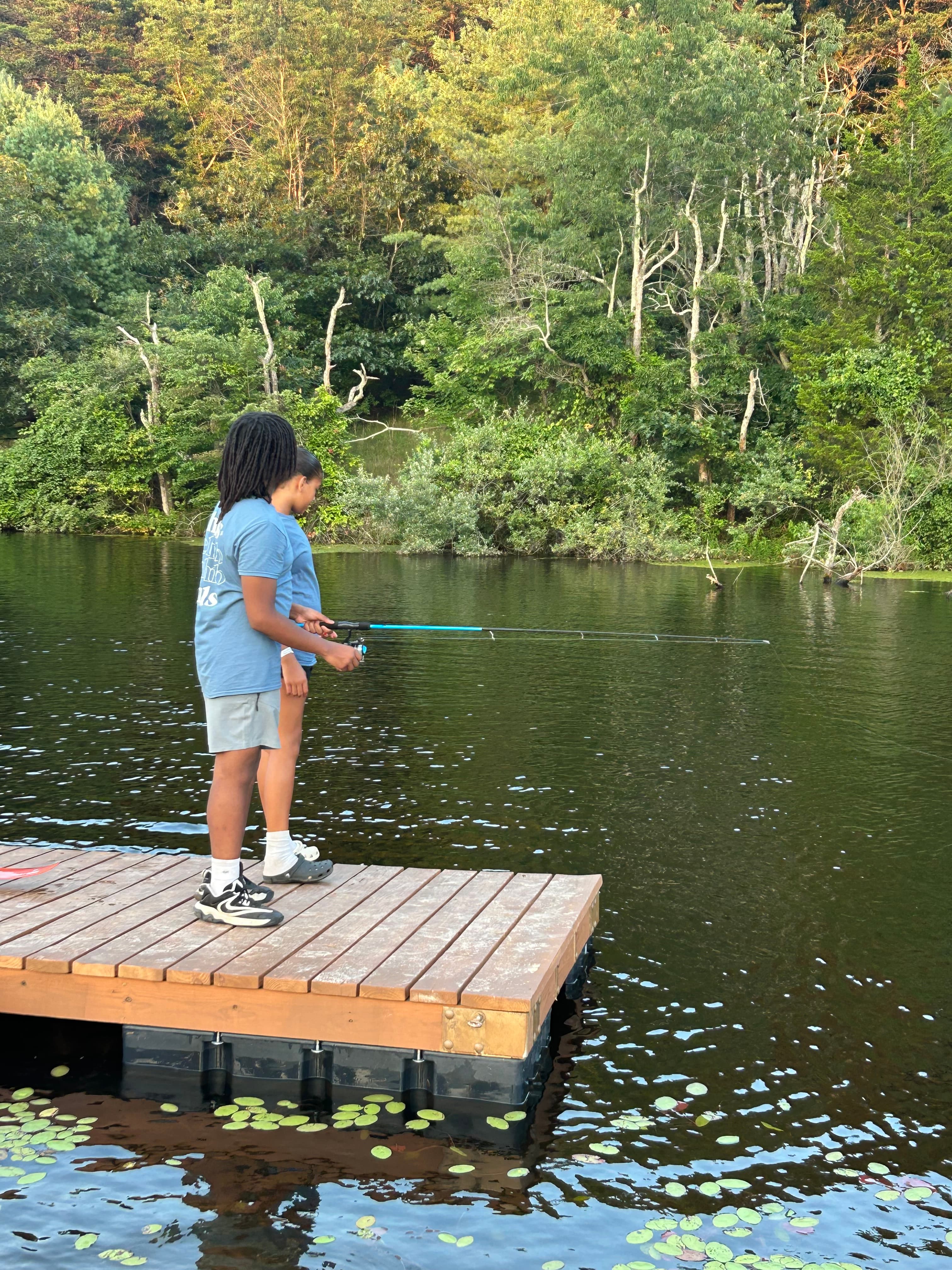 A young person fishes from a dock at camp
